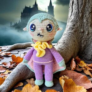 Patrón amigurumi de Vladkie el vampiro kawaii con capa morada frente a un castillo embrujado